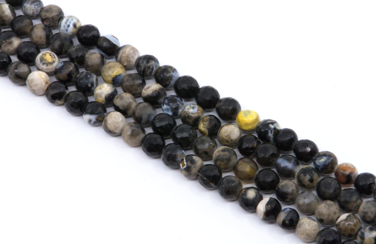 Multiple strands of polished faceted round gemstone beads in black, gray, brown, and white , arranged diagonally on a white background.