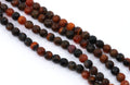 Four strands of faceted round agate beads in a mix of  orange and black with natural stone patterns, laid out diagonally on a white background.