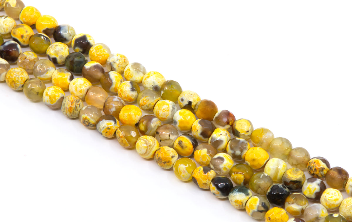 Four diagonal strand of polished round gemstone beads in golden orange and black on a white background.