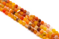 Multiple strands of round faceted agate bead charms in warm orange, yellow, red, and brown tones, arranged diagonally on a plain white background.