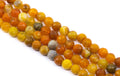 Four strands of faceted round gemstone beads in warm earthy tones, including orange, yellow and gray arranged diagonally on a white background.
