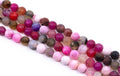 four strands of polished round faceted agate beads in various colors and , including pink, red, purple, brown, and smoky gray, arranged diagonally on a white background.