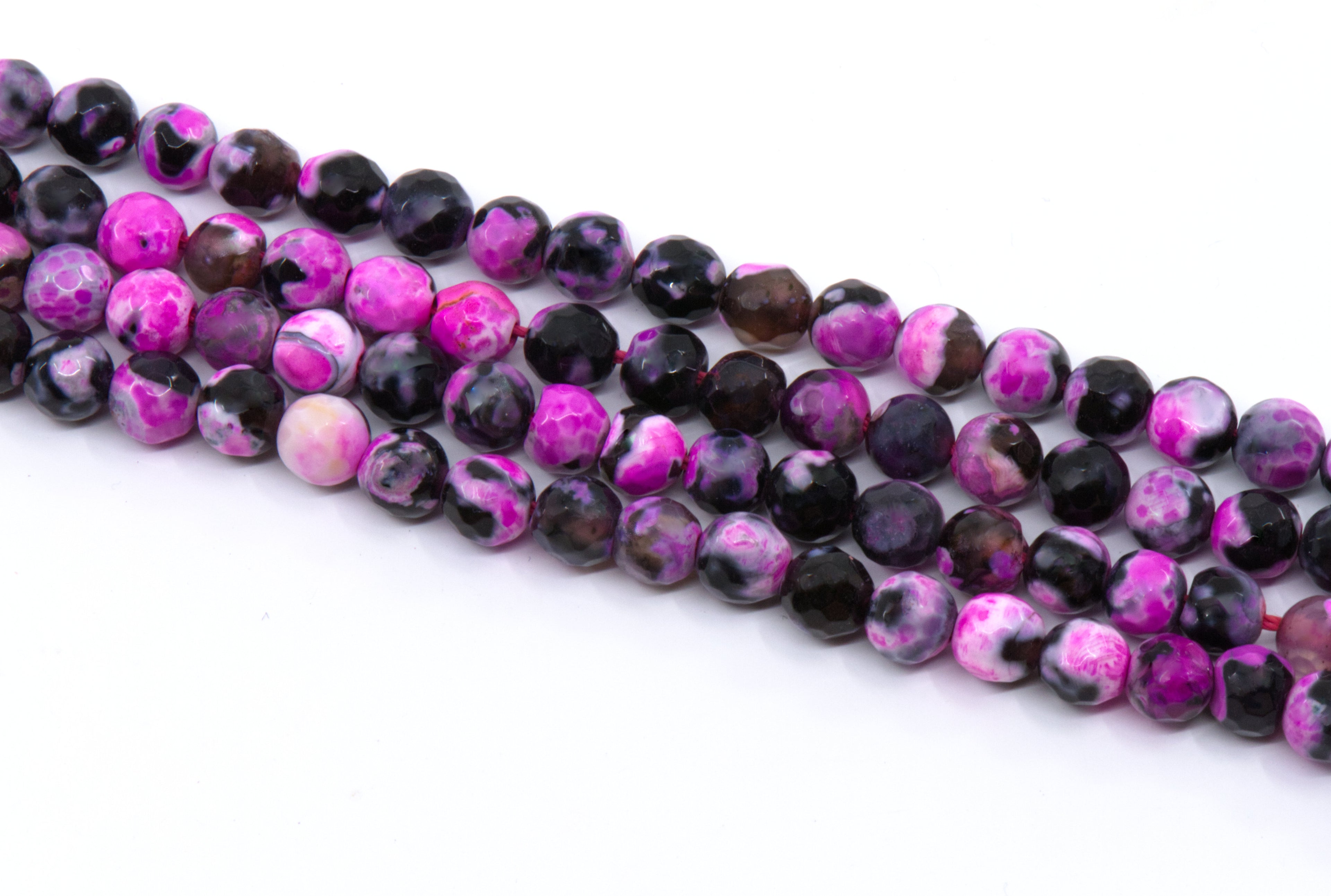 four strands of round faceted agate beads in pink and black, arranged diagonally on a plain white background.