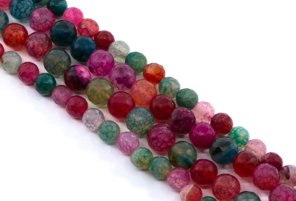 Multiple strands of faceted round gemstone beads in assorted colors, including pink, red and green arranged diagonally on a white background.