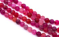 Four strands of faceted round gemstone beads in shades of pink, magenta, and red, arranged diagonally on a white background.