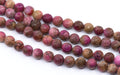 Multiple strands of polished round faceted agate beads in pinkish-red and brown , arranged diagonally on a white background.