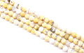 four strands of faceted round agate beads, featuring a mix of yellow and white colors, arranged diagonally on a white background.