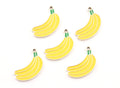 Five yellow banana-shaped charms with green stems and gold metal loops, arranged on a plain white background.