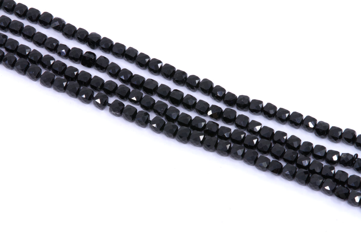 four strands of black tourmaline cube beads arranged diagonally on a plain white background.