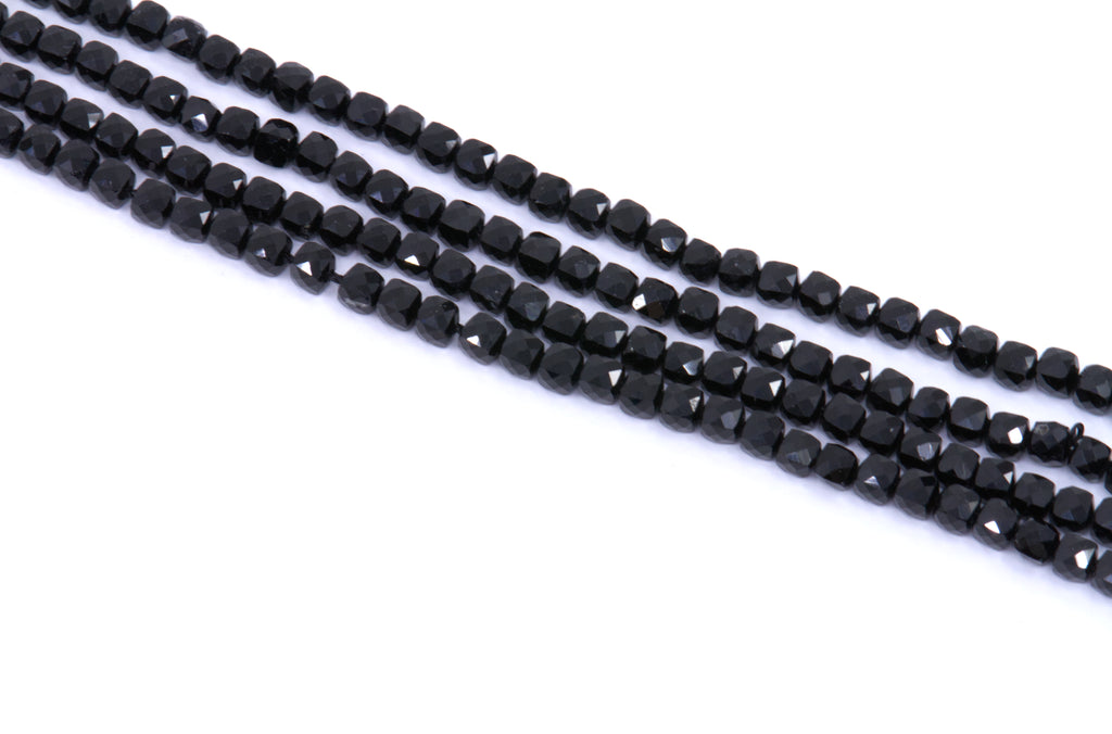 four strands of black tourmaline cube beads arranged diagonally on a plain white background.
