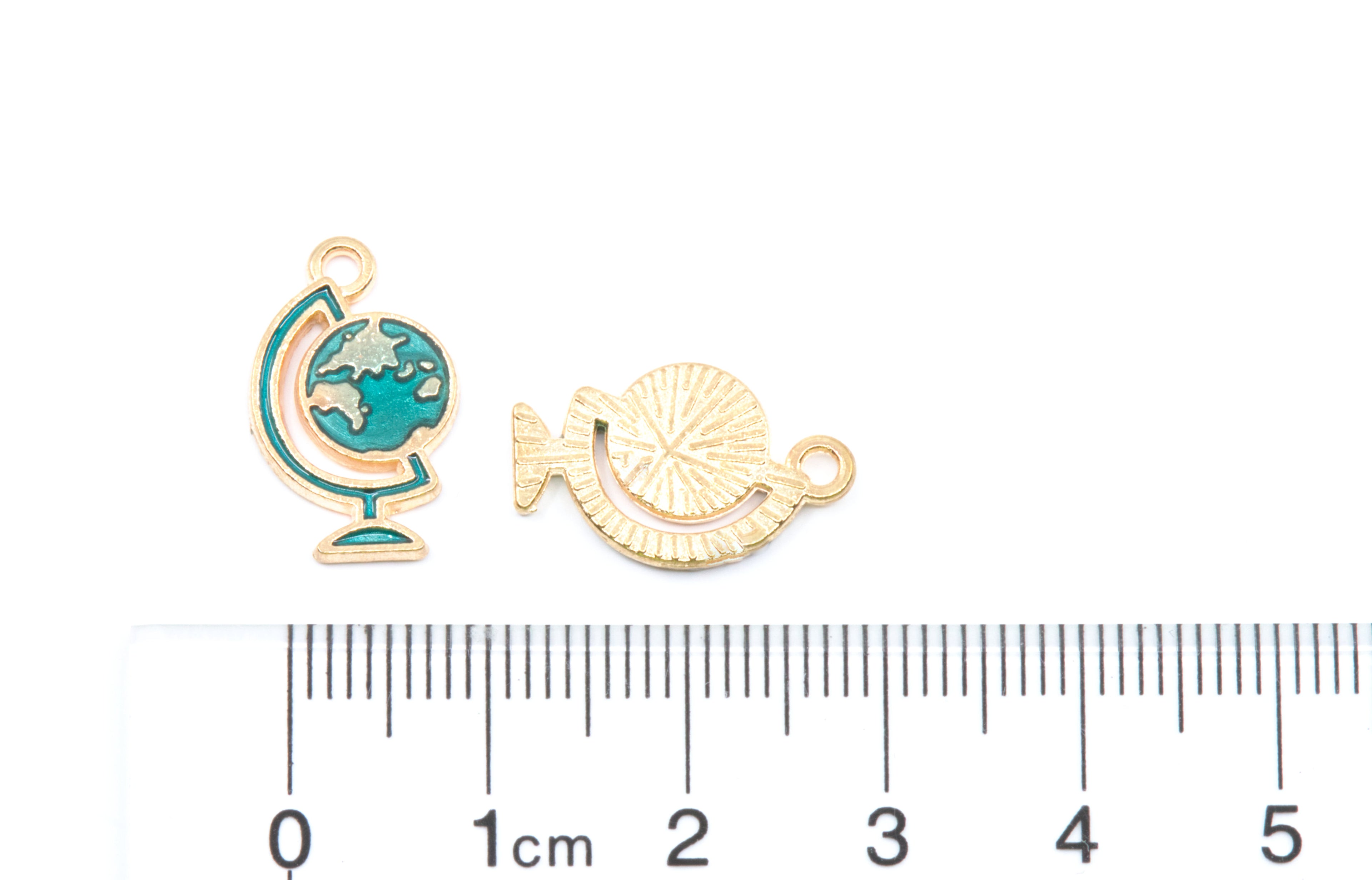 Two blue globe  gold-tone jewelry charms next to a  cm ruler for scale on a white background.