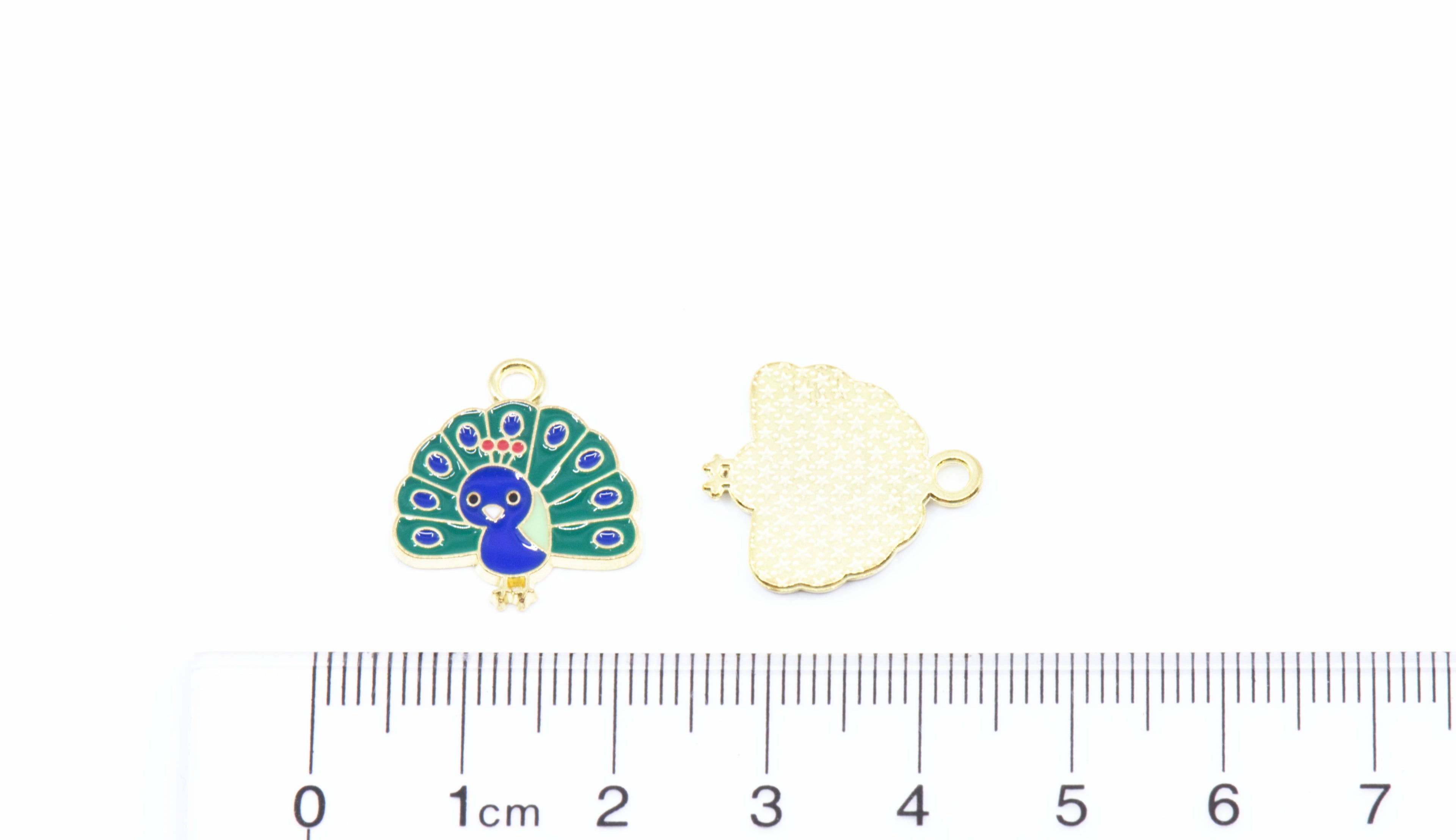 Two peacock jewelry charms shown on a white background with a ruler at the bottom for scale: 