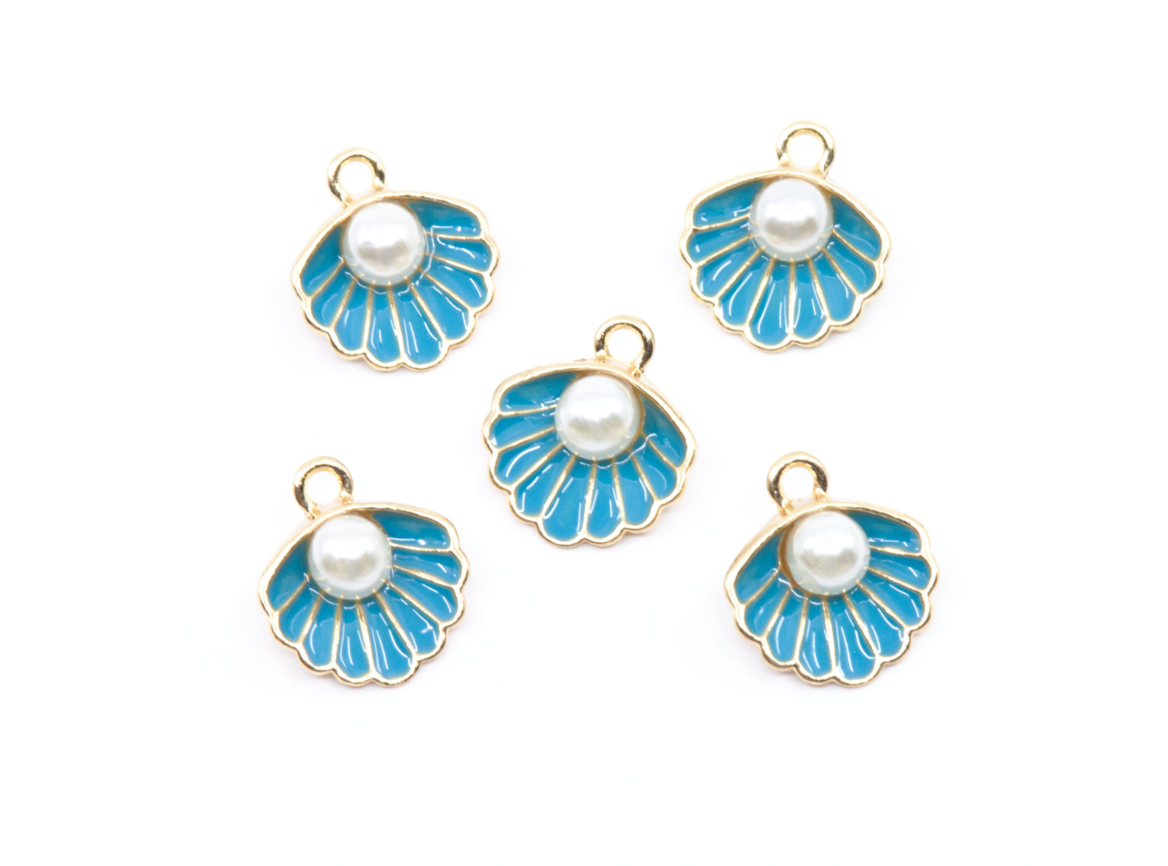 Five shell-shaped jewelry charms with bright blue enamel, white faux pearls, and gold-tone metal borders, arranged on a plain white background.