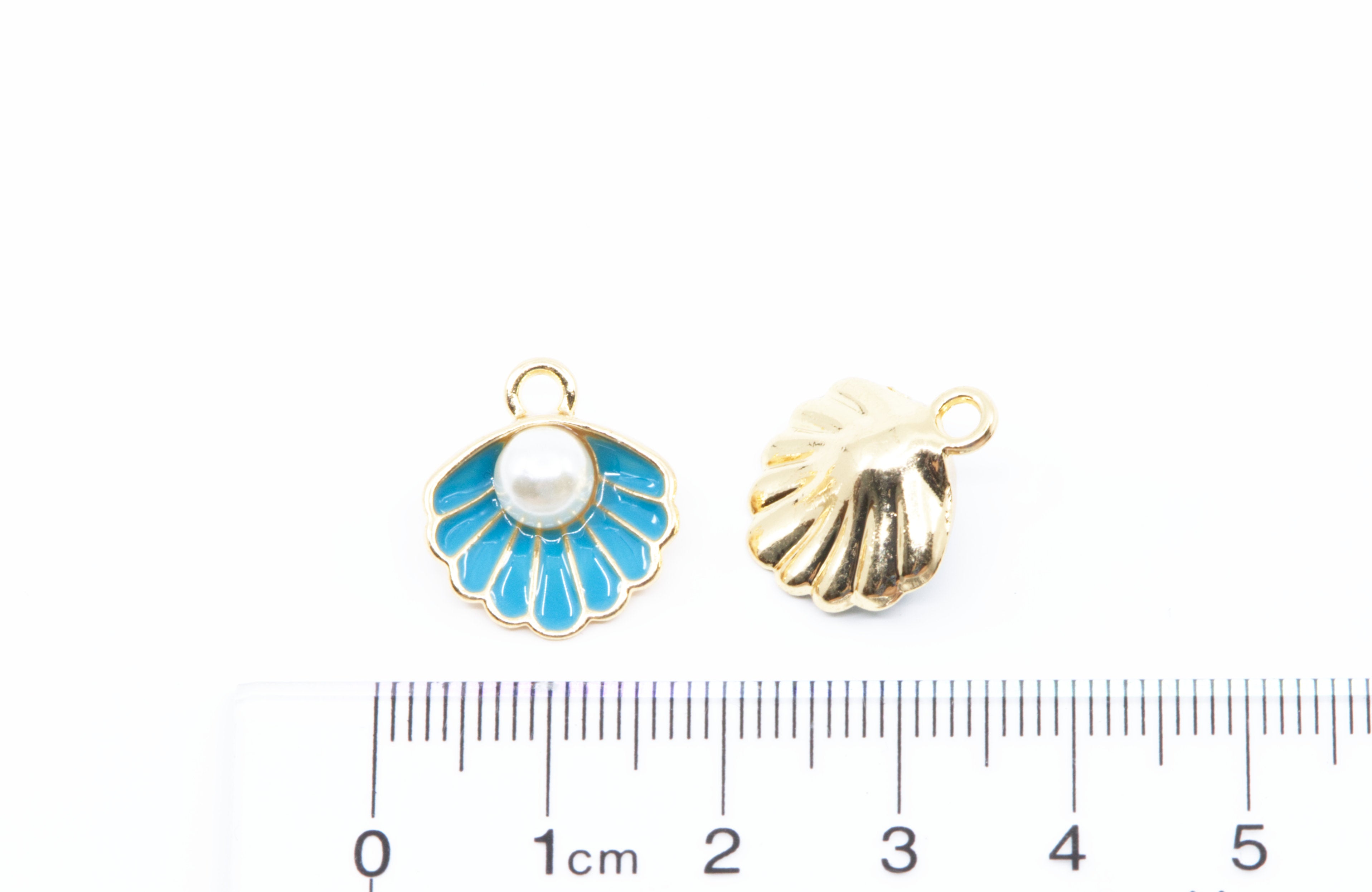 Two small shell-shaped jewelry charms or pendants shown on a white background with a ruler at the bottom for scale. 