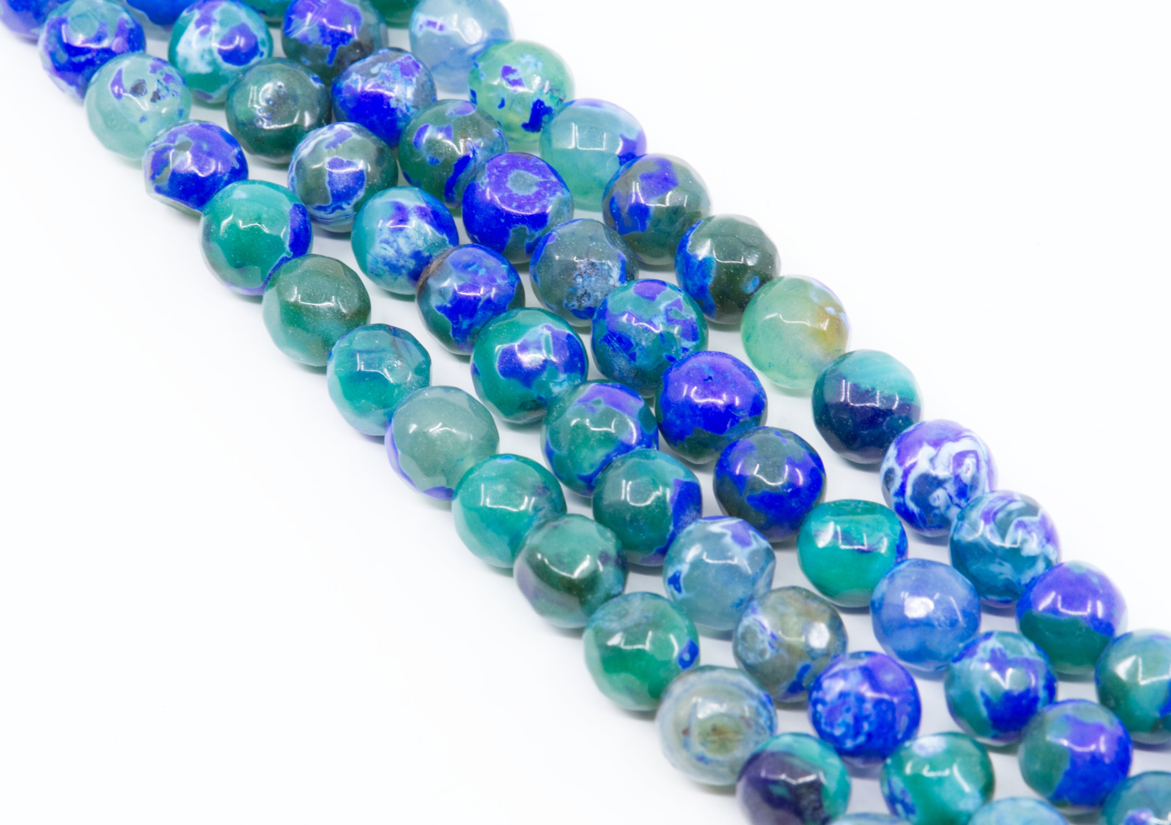 Faceted round agate beads in blue, teal, and green, arranged in diagonal strands on a white background.