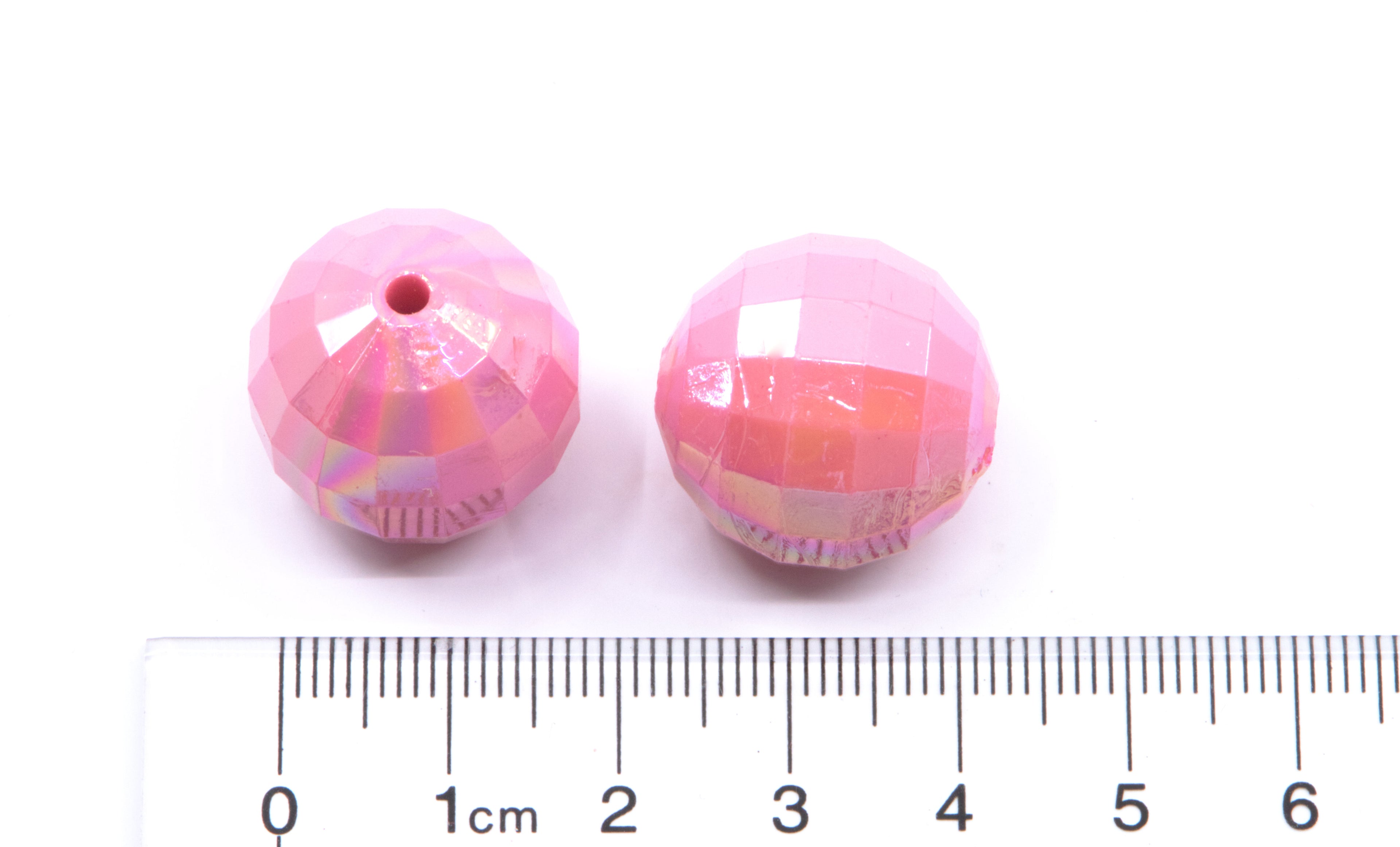 Two pink beads on a white background, accompanied by a ruler for scale.