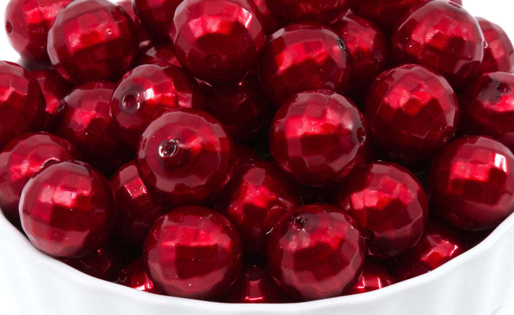 A close-up of  faceted red glass beads piled in a white bowl.