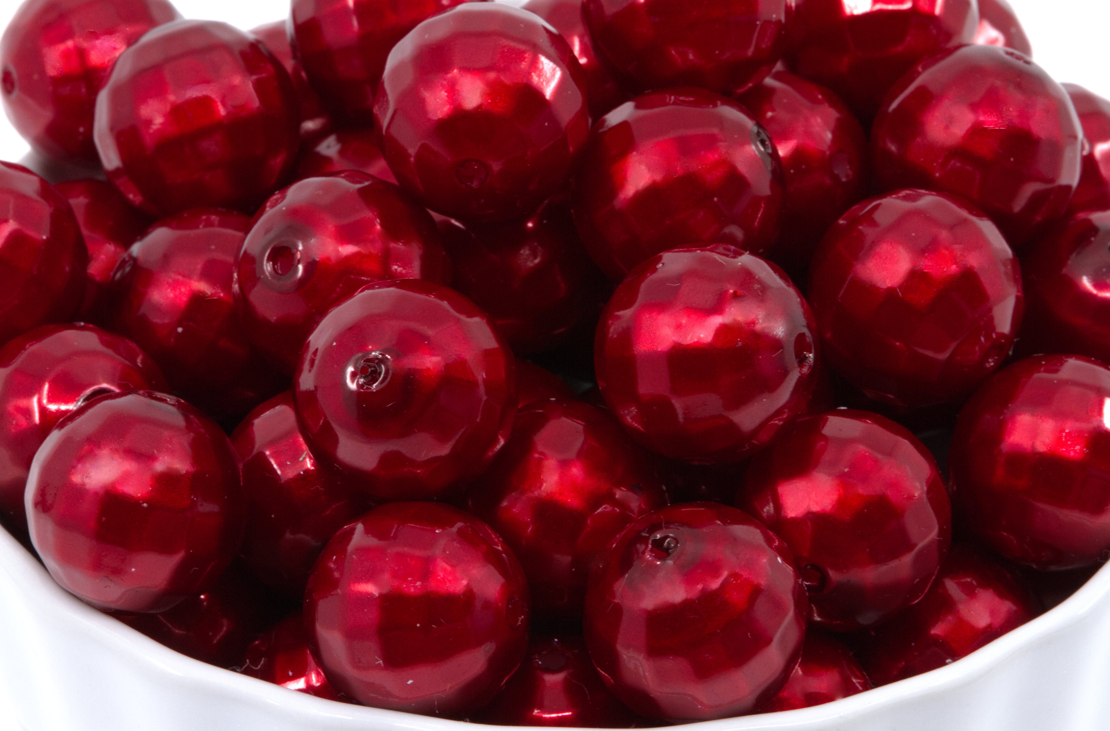 A close-up of  faceted red glass beads piled in a white bowl.