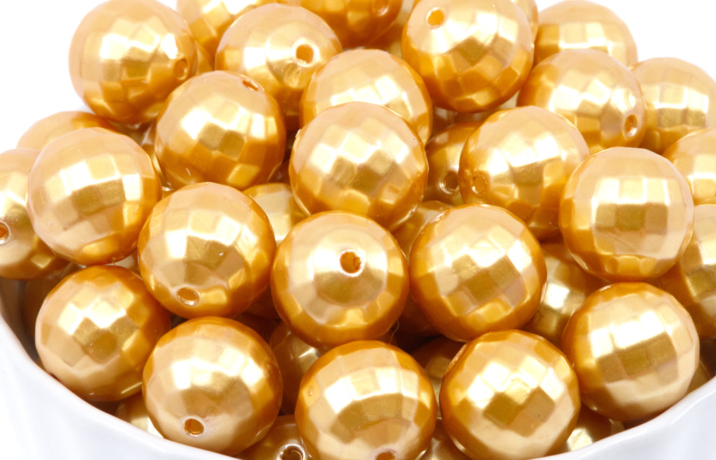 A pile of shiny metallic gold faceted round beads with holes, shown close up in a white container against a white background.