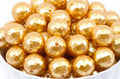 A pile of shiny metallic gold faceted round beads with holes, shown close up in a white container against a white background.