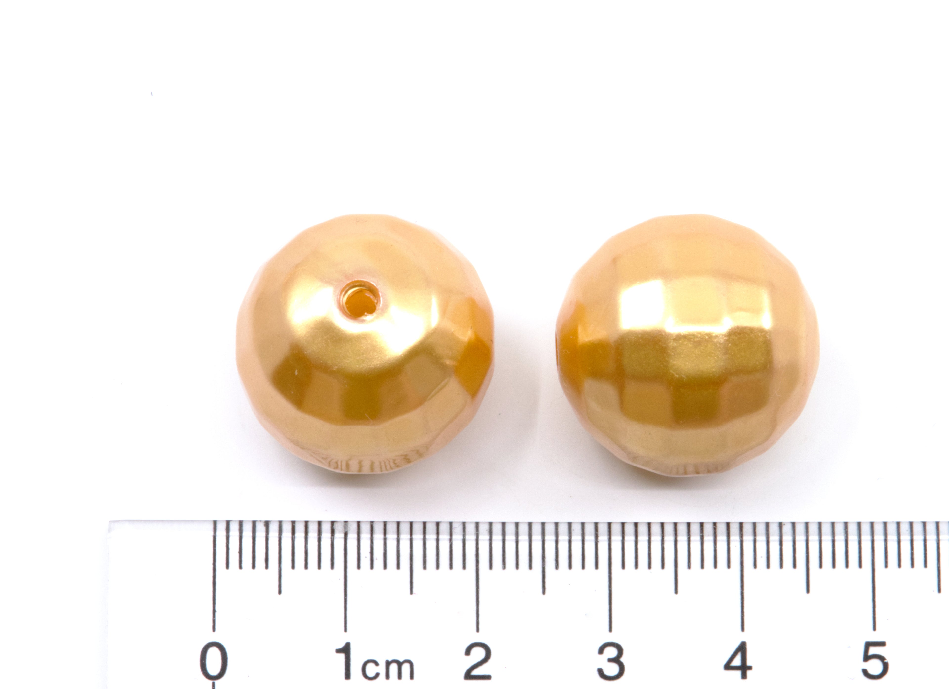 Two faceted gold bubblegum beads shown next to a cm ruler for scale on a white background.