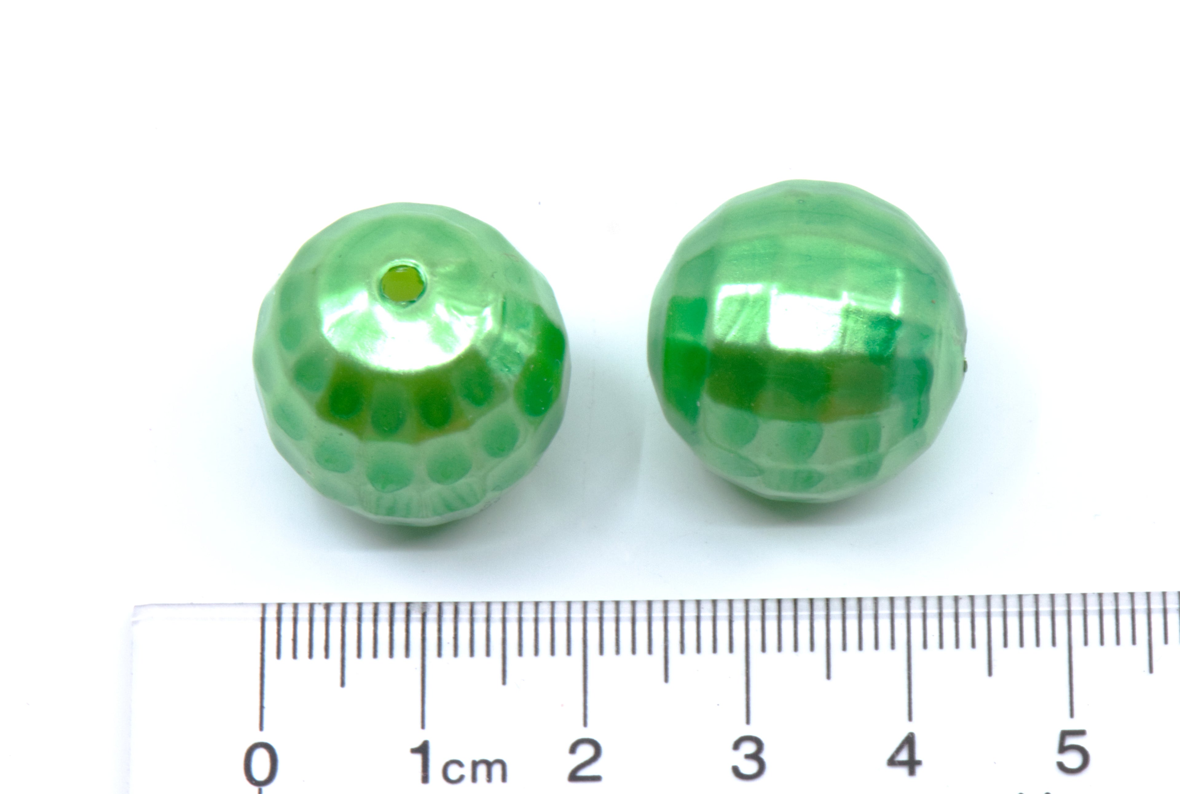 Two green faceted glass beads shown next to a cm ruler for scale on a white background.