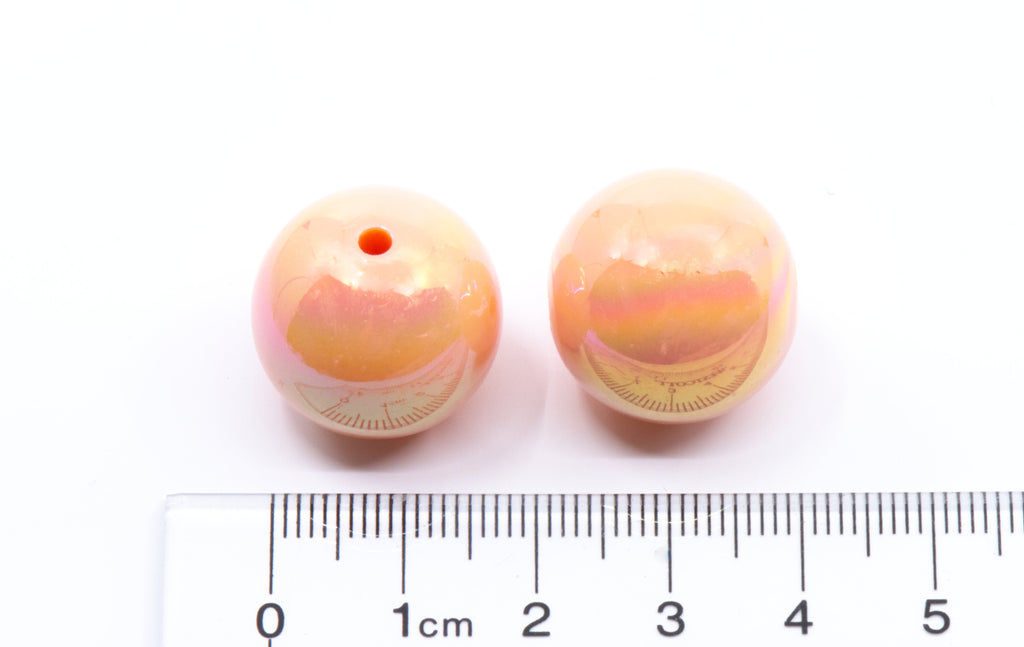 Two orange iridescent beads with a ruler for scale on a white background