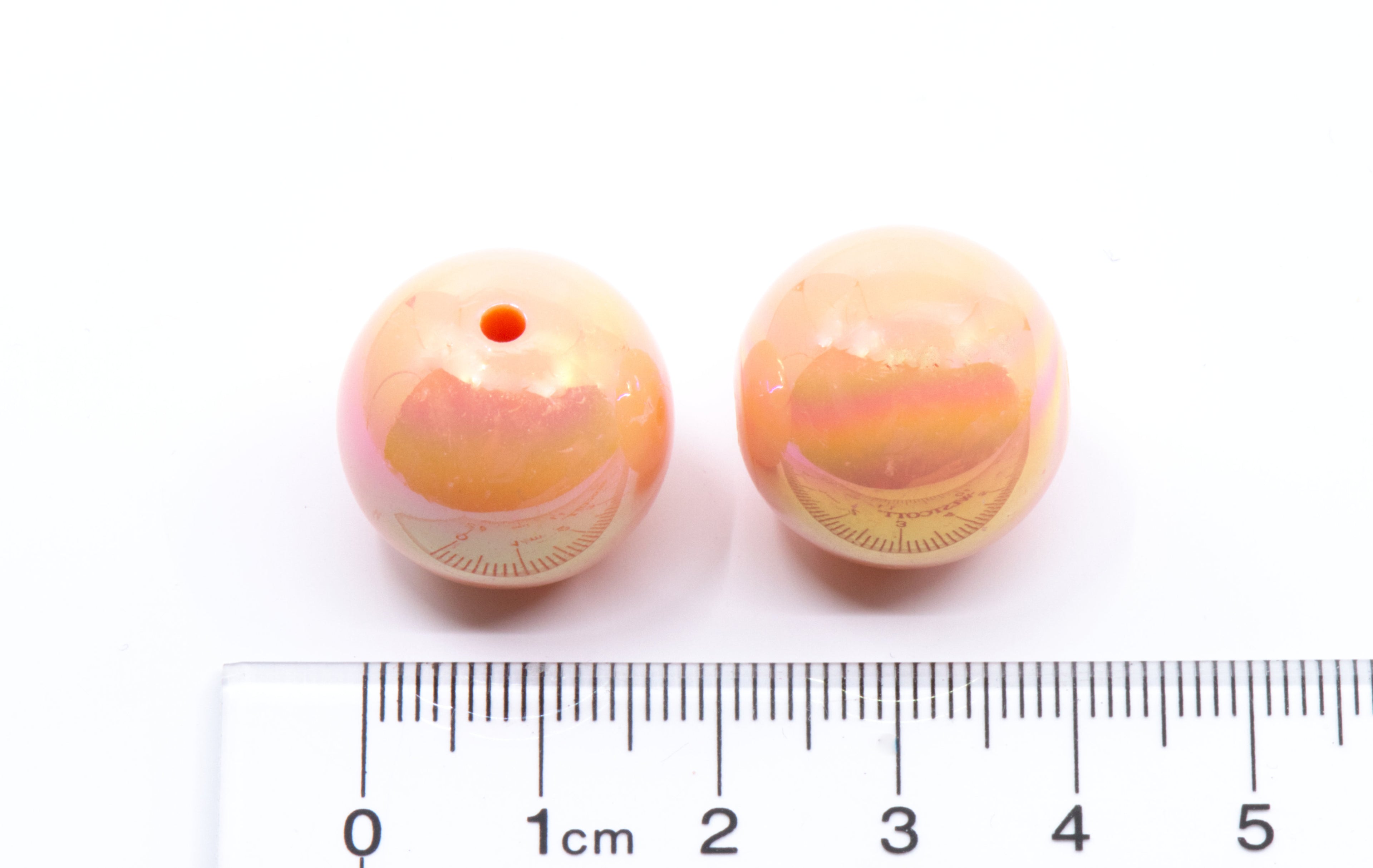 Two orange iridescent beads with a ruler for scale on a white background