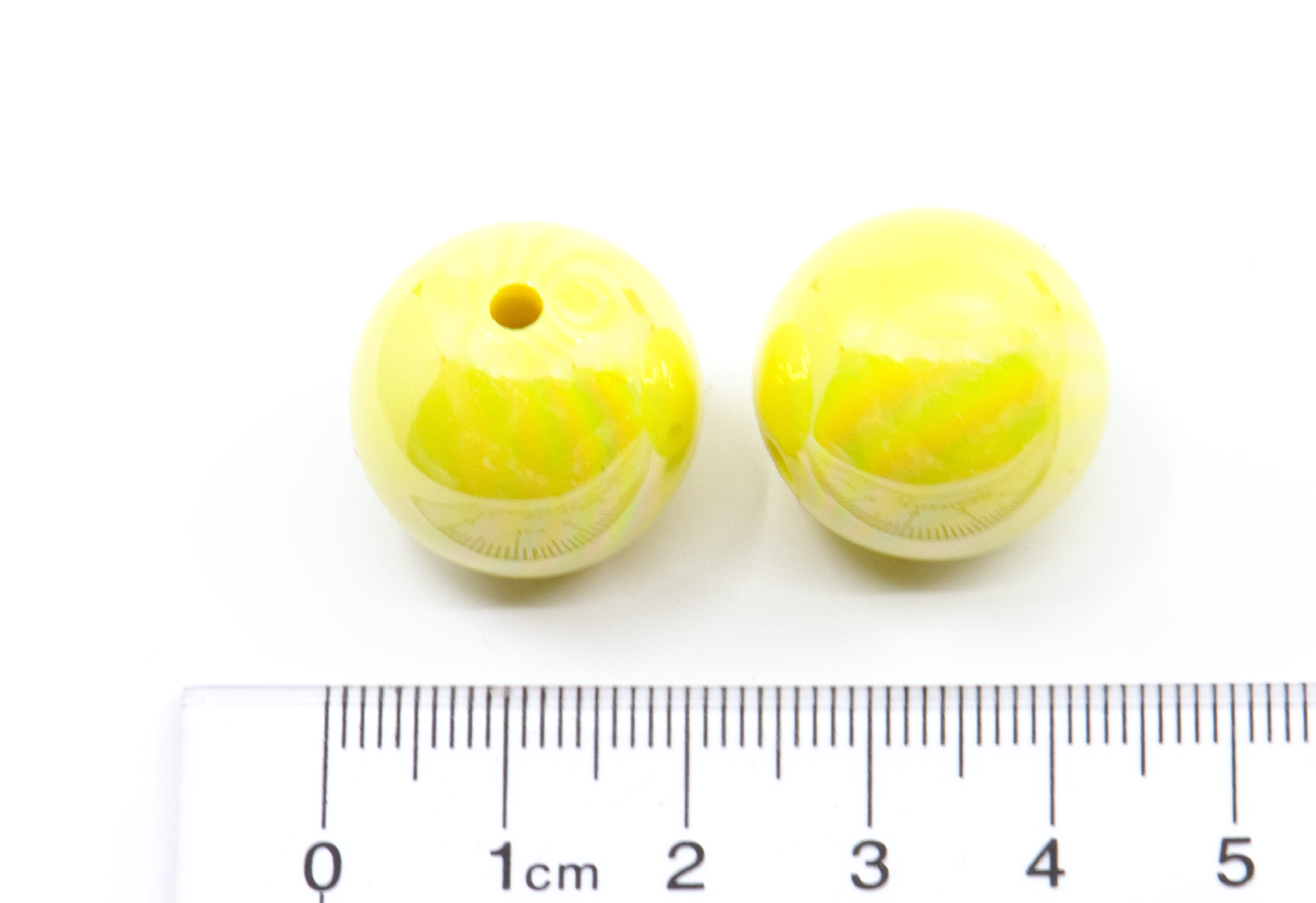 Two yellow iridescent beads next to a ruler for size reference on a white background