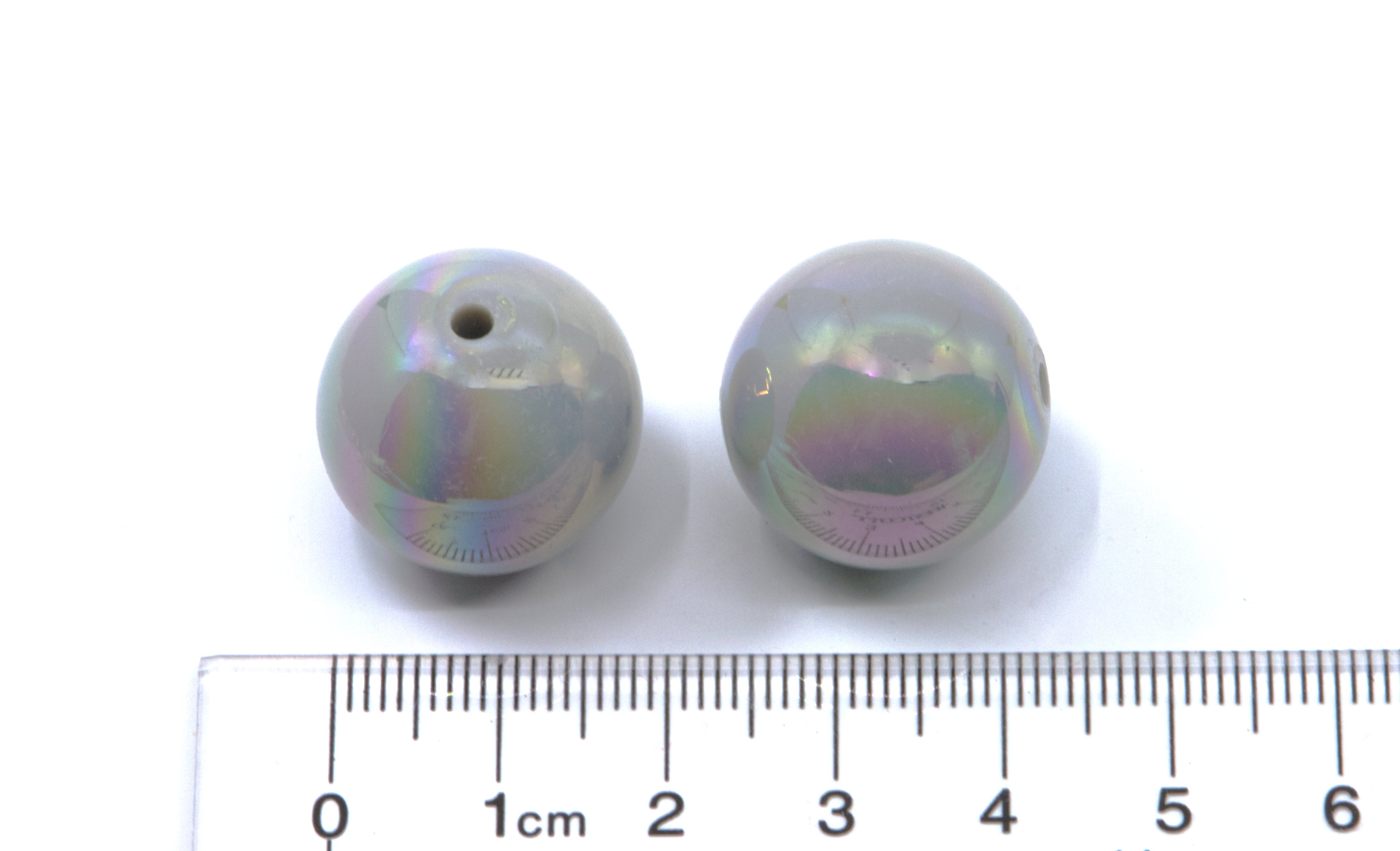 Two iridescent beads with a ruler for scale on a white background