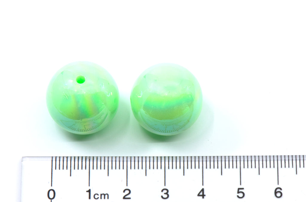 two green iridescent beads with a ruler for scale on a white background