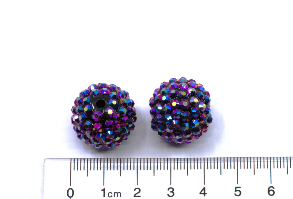 Two round metallic indigo AB rhinestone bubblegum beads, shown next to a cm ruler for scale on a white background.
