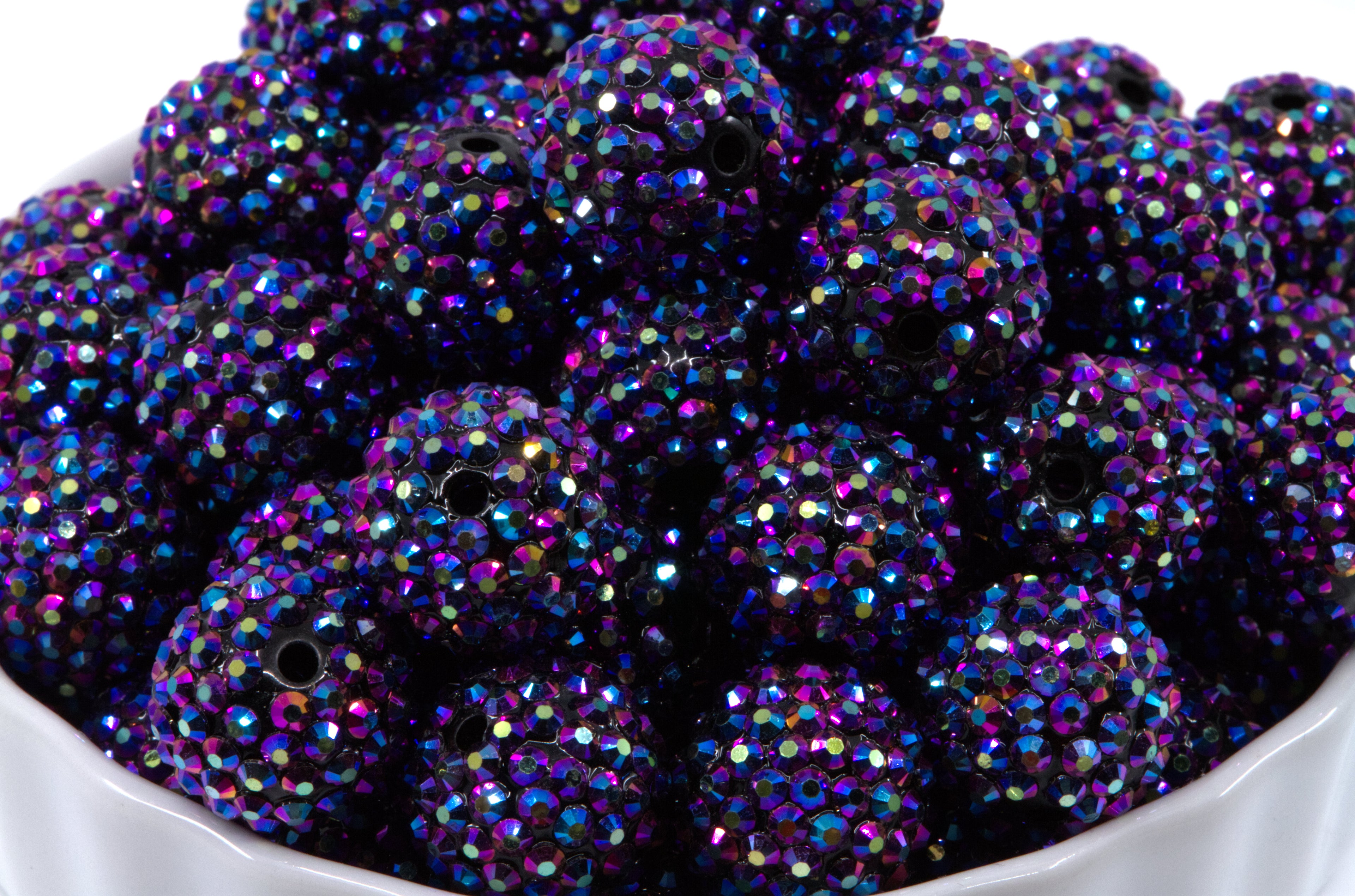 A close-up of round metallic indigo AB rhinestone bubblegum beads, piled inside a white bowl against a white background.