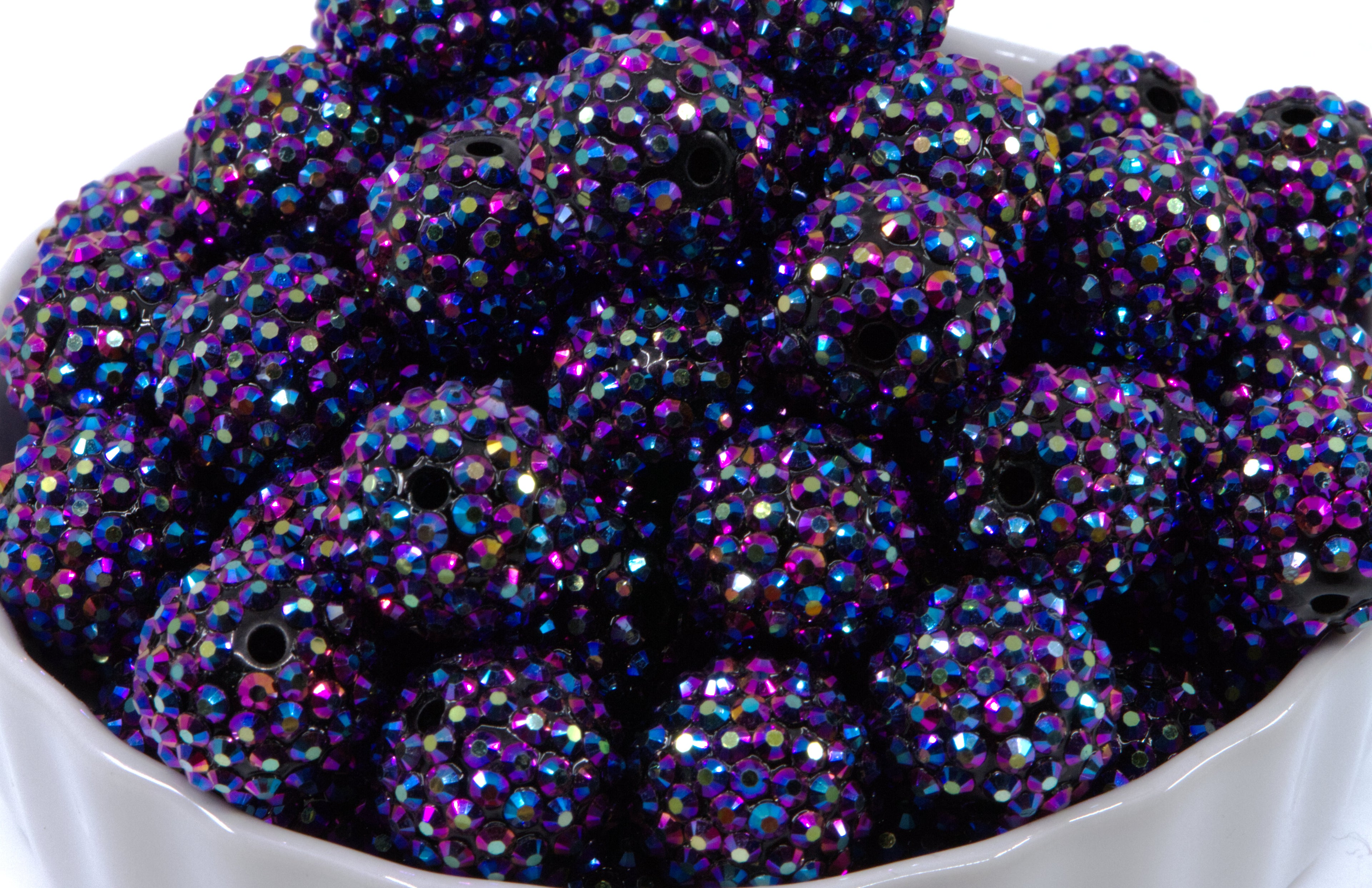 A close-up of round metallic indigo AB rhinestone bubblegum beads, piled inside a white bowl against a white background.