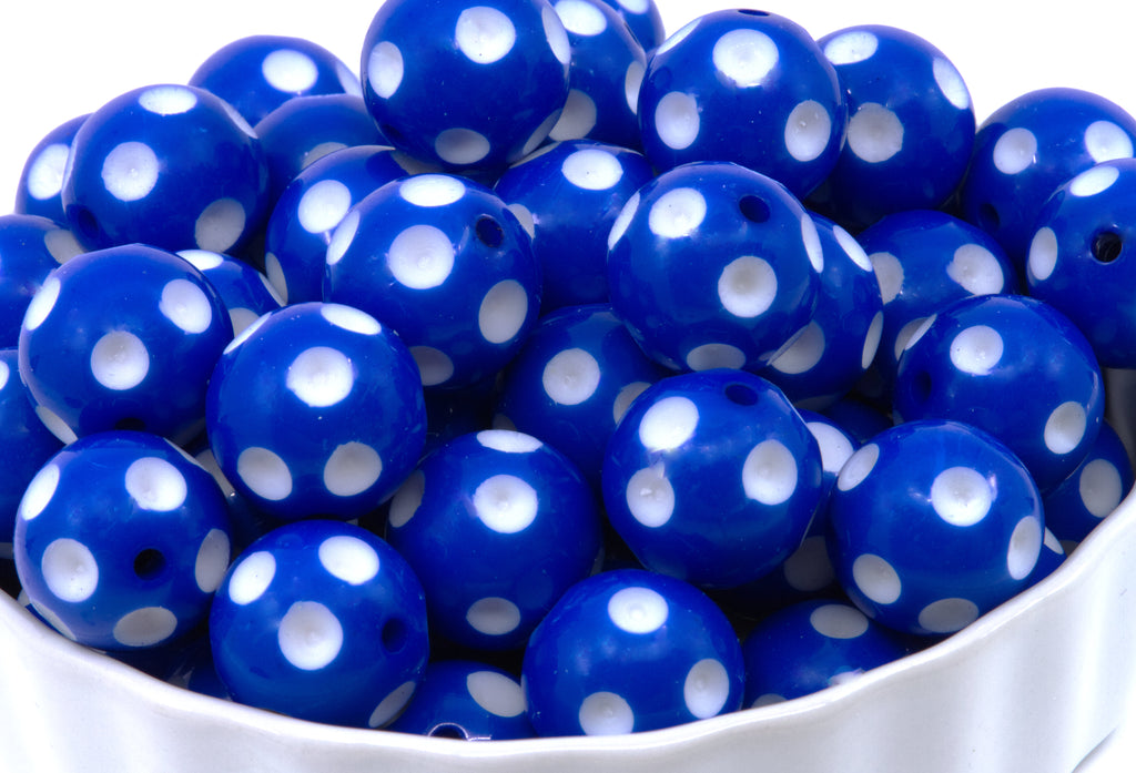 A close-up of blue round beads with white polka dots piled in a white bowl against a white background.