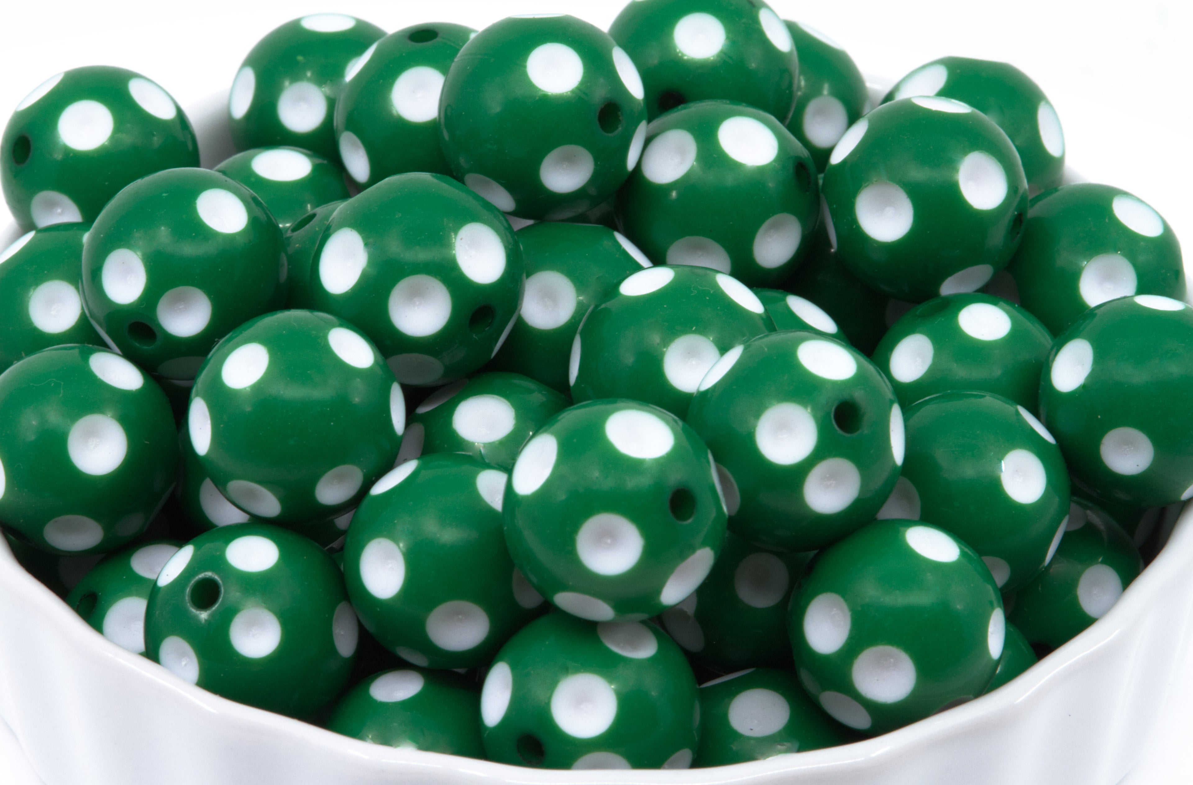 Green round beads with white polka dots, piled inside a white bowl against a white background.