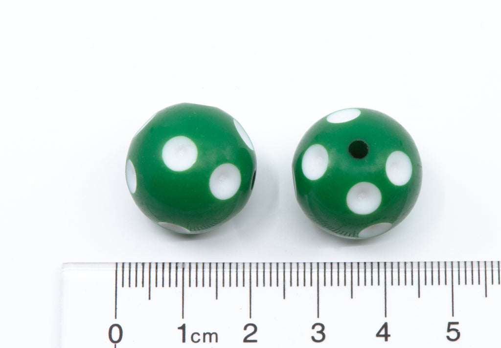 Two green glass beads with white polka dots shown next to a cm ruler for scale on a white background.