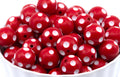 A pile of red round beads with white polka dots, shown in a white bowl against a white background.