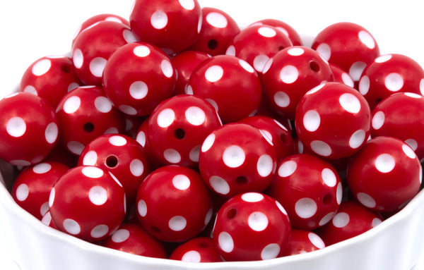 A pile of red round beads with white polka dots, shown in a white bowl against a white background.