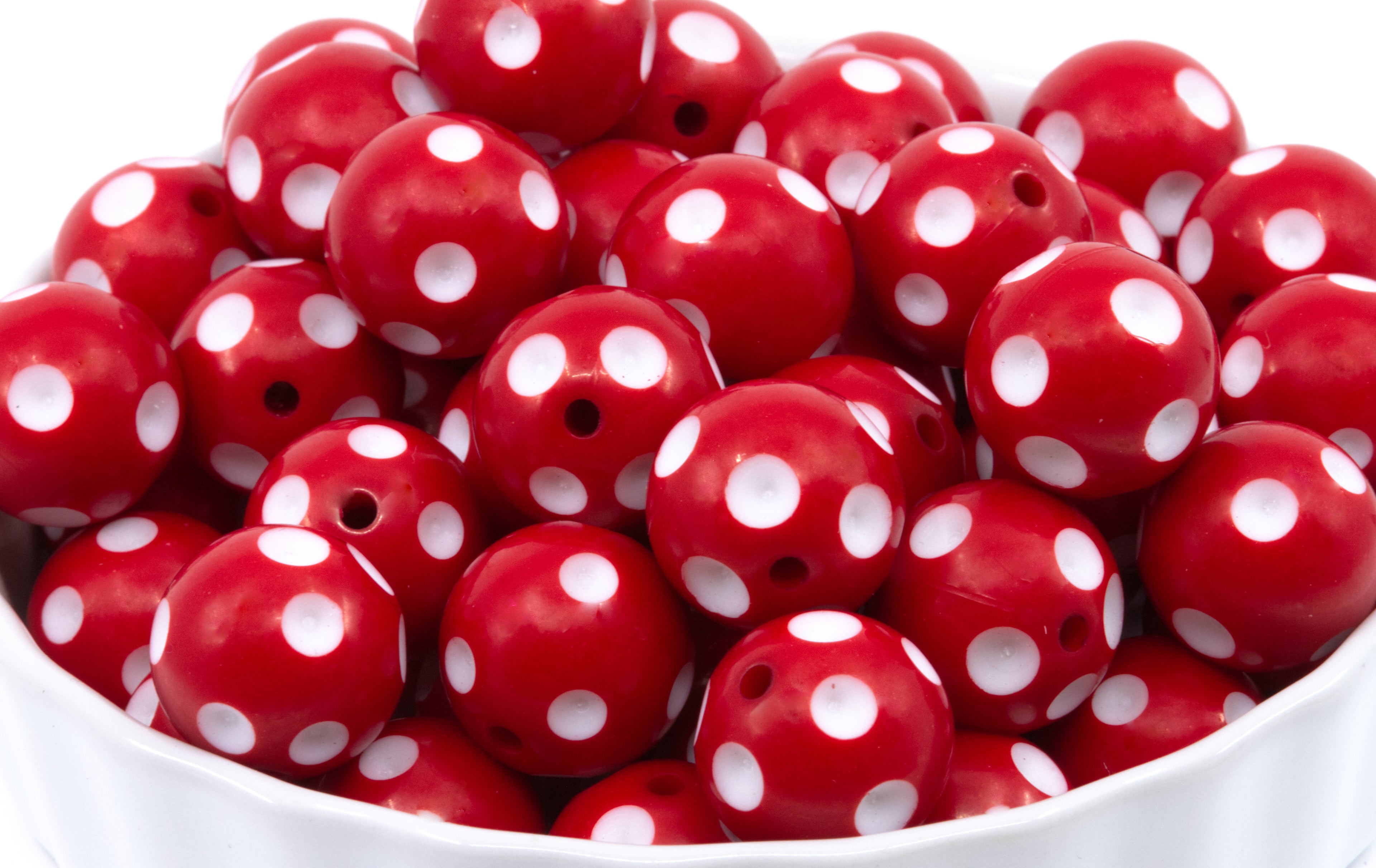 A pile of red round beads with white polka dots, shown in a white bowl against a white background.