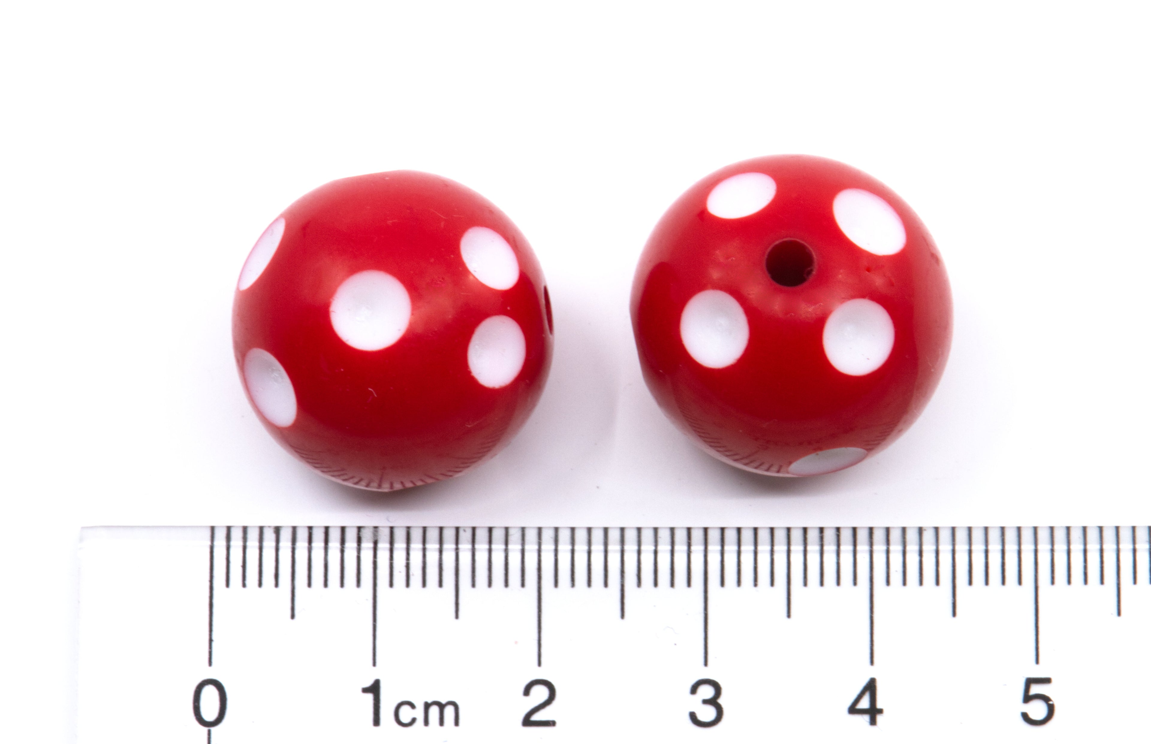 Two red beads with white polka dots, shown next to a cm ruler for scale on a white background.