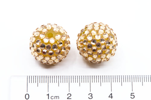 Two round gold-toned rhinestone-covered beads shown next to a cm ruler for scale on a white background.