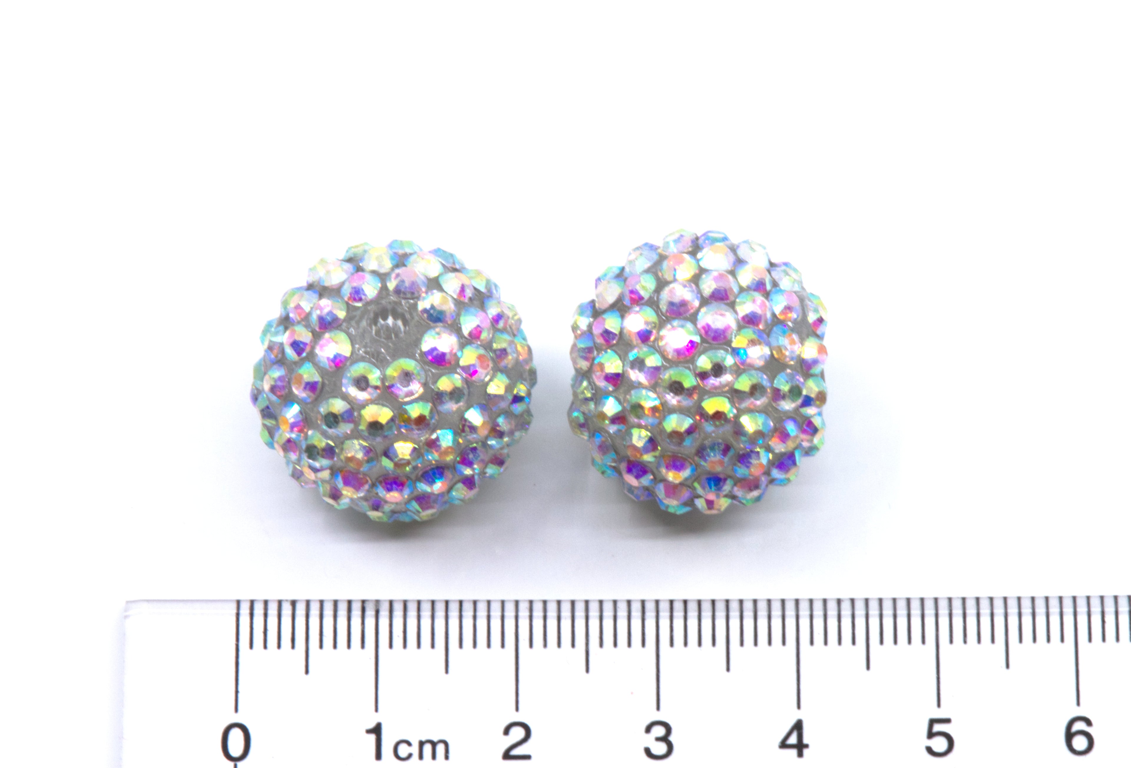 Two round crystal AB rhinestone beads, shown next to a cm ruler for scale on a white background.
