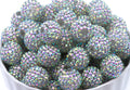 A pile of round, crystal AB rhinestone beads sitting in a white bowl against a white background.