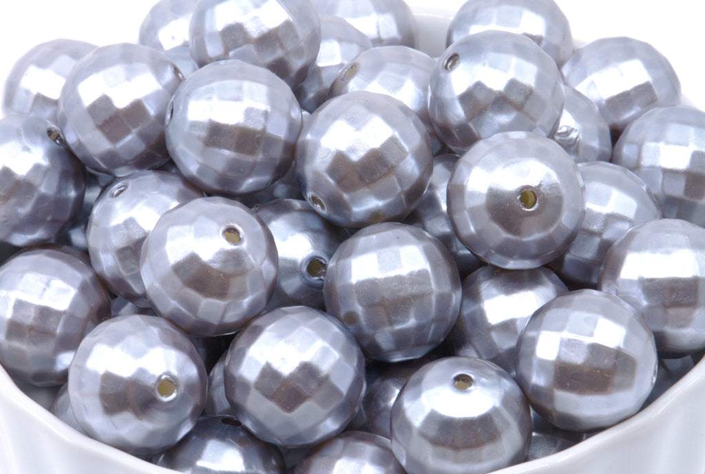 A close-up of shiny metallic silver faceted beads with a central hole, piled inside a white container against a white background.