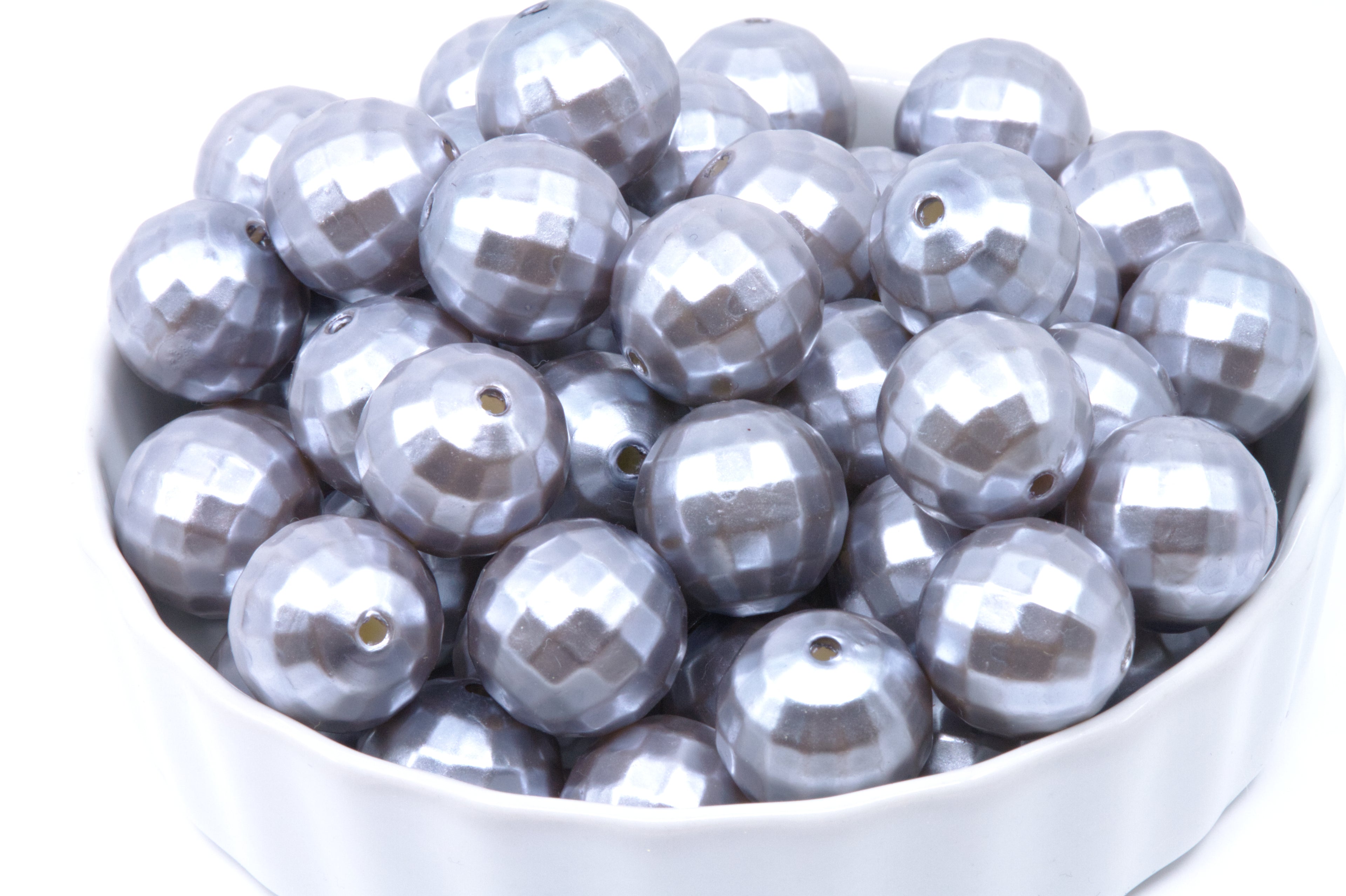 A white bowl filled with faceted silver beads on a plain white background.