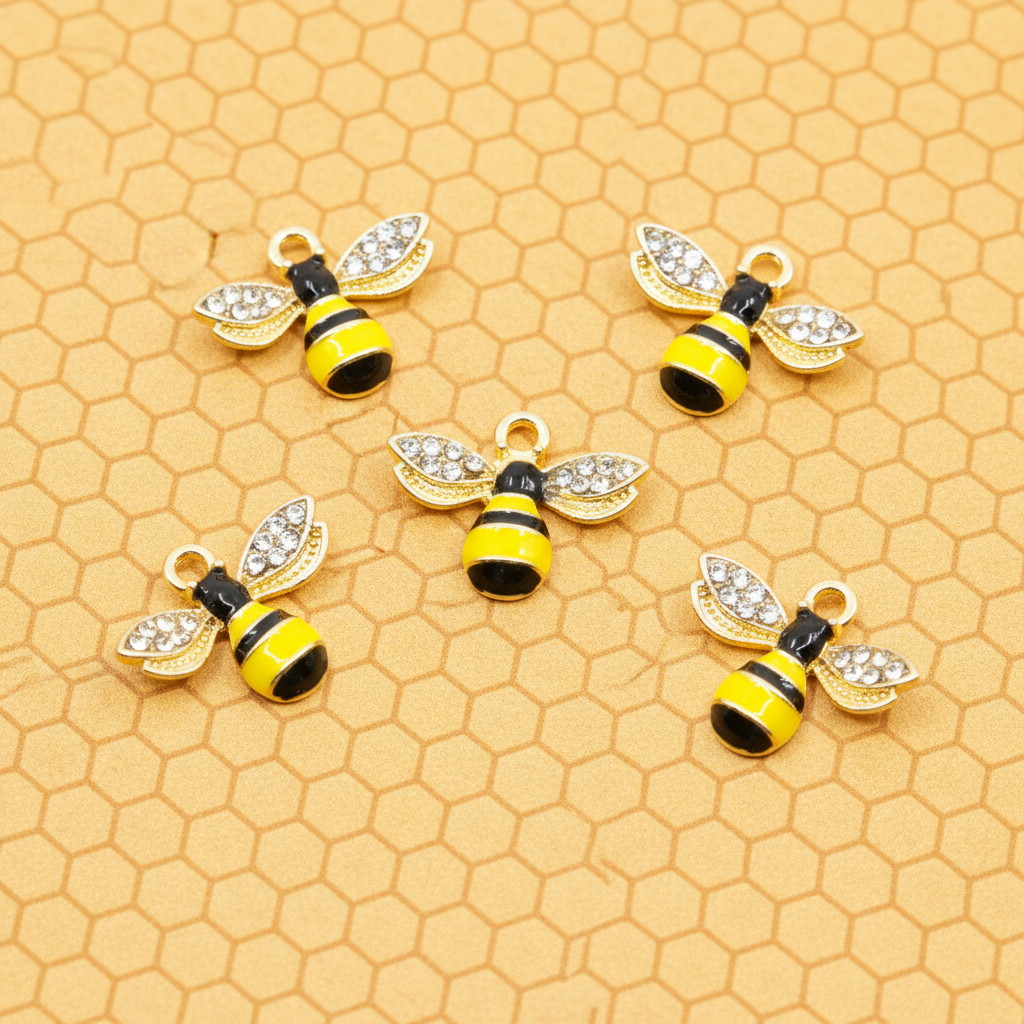 Five gold bumblebee jewelry charms with black and yellow enamel stripes and clear rhinestone wings, arranged on a honeycomb-patterned gold background.