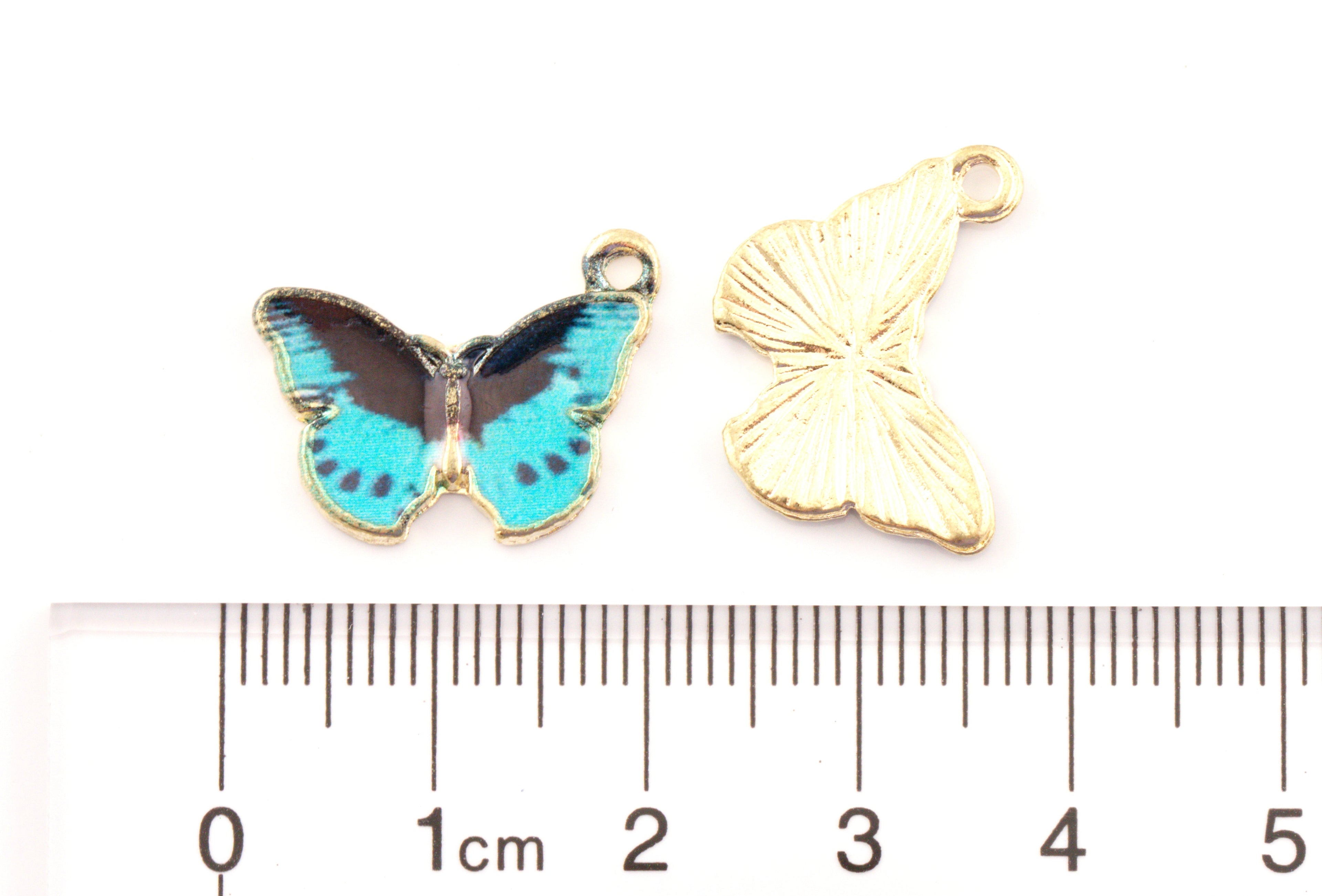 Two butterfly-shaped jewelry charms shown on a white background with a ruler below for scale. 