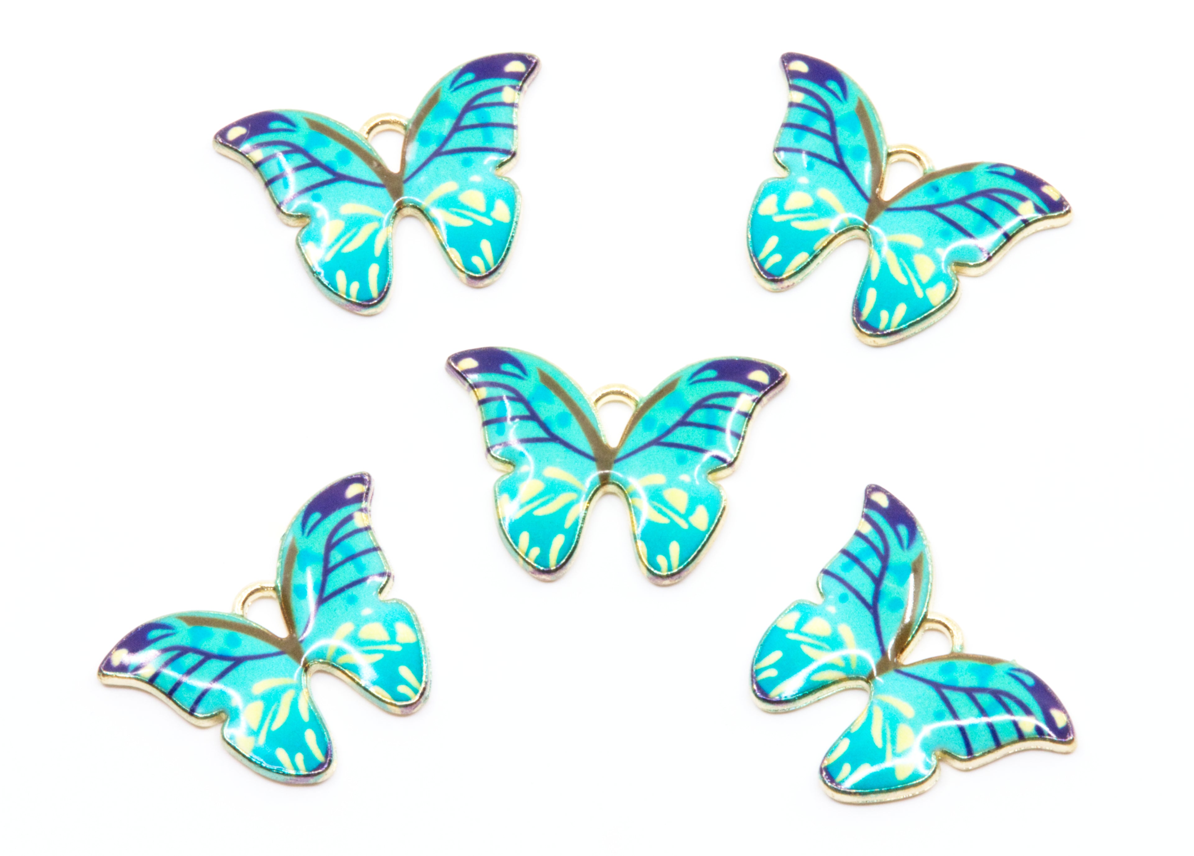 Five butterfly-shaped jewelry charms with blue and green enamel wings and gold-tone edges, arranged on a plain white background.