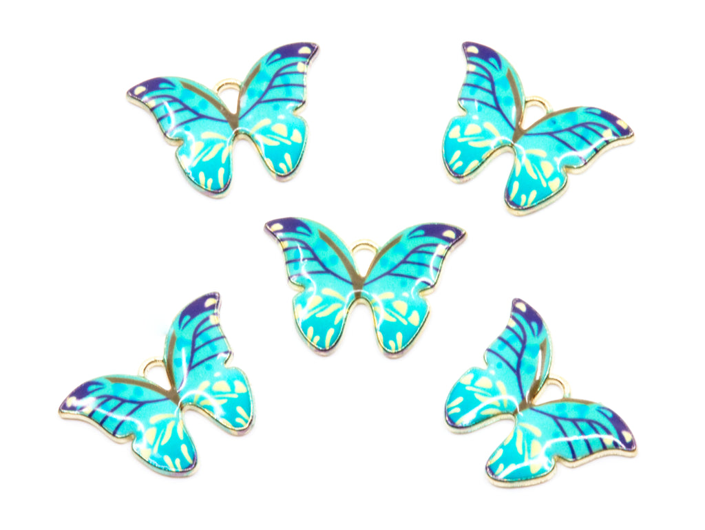 Five butterfly-shaped jewelry charms with blue and green enamel wings and gold-tone edges, arranged on a plain white background.
